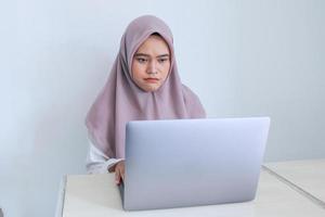 Young Asian Islam woman wearing headscarf is serious look to the laptop. Indonesian woman on gray background photo