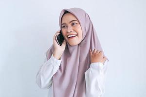 Young Asian Islam woman wearing headscarf is happy and smile when talking on the phone. Indonesian woman on gray background photo