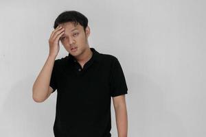 Portrait of young asian man isolated on grey background suffering from severe headache, pressing fingers to temples, closing eyes to relieve pain with helpless face expression photo
