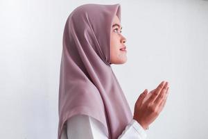 Asian Islam Muslim woman in headscarf and hijab prays with her hands up in air with smile face. Indonesian woman. Religion praying concept isolated on grey background photo