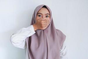 Young Asian Islam woman wearing headscarf is shocked with her hands covering her mouth. Indonesian woman on gray background photo