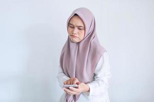 Young Asian Islam woman wearing headscarf is sad and cry in what she see on the smartphone. Indonesian woman on gray background photo