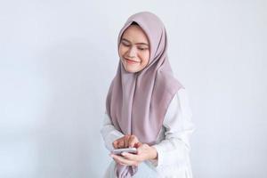 Young Asian Islam woman wearing headscarf is smile and happy in what she see on the smartphone. Indonesian woman on gray background photo