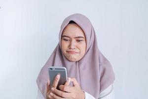 la joven islámica asiática que lleva pañuelo en la cabeza está triste y llora por lo que ve en el smartphone. mujer indonesia sobre fondo gris foto