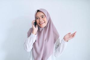 Young Asian Islam woman wearing headscarf is happy and smile when talking on the phone. Indonesian woman on gray background photo