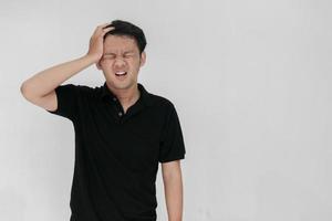 Portrait of young asian man isolated on grey background suffering from severe headache, pressing fingers to temples, closing eyes to relieve pain with helpless face expression photo