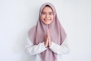 Young Asian Islam woman wearing headscarf gives greeting hands at with a big smile on her face. Indonesian woman on gray background. Eid Mubarak greeting photo