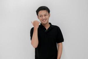 feliz y sonrisa de un joven asiático con un punto de mano en el espacio vacío. indonesia hombre usar camisa negra aislado fondo gris foto