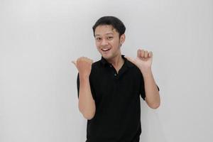 Happy and smile of young Asian man with hand point on empty space. Indonesia Man wear black shirt Isolated grey background photo