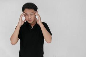 Portrait of young asian man isolated on grey background suffering from severe headache, pressing fingers to temples, closing eyes to relieve pain with helpless face expression photo