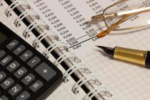 Financial report, a fountain pen, glasses and paper with numbers on the table in the office. A paper sheet full of business data. Accounts number on the data paper. Business documents. Close-up
