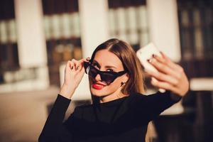 lindo retrato de una mujer joven y atractiva sosteniendo un teléfono inteligente y tomando un retrato selfie. foto