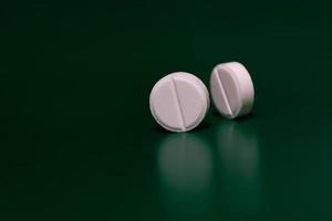 Two round white pills on a green background, stand on their side. Medical theme photo