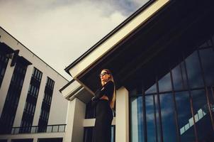 modelo atractivo en gafas de sol de pie cerca del centro de negocios foto