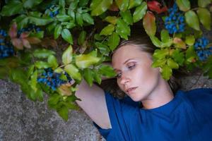 A woman with blue eyes lies on a stone against a background of flowers. photo