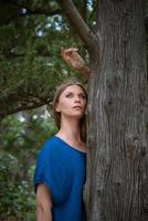 una mujer mira desde detrás de un árbol y mira a lo lejos. foto