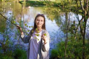 una chica con gafas de sol cerca del lago, sosteniendo una rama de árbol en sus manos foto