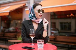 A beautiful woman is sitting in a cafe on the street with a glass of wine photo