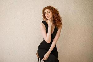 A red-haired young woman poses against a wall, a place for an inscription . Stylish and fashionable girl photo