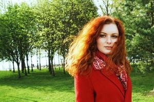 Portrait of a cute woman in a red coat against the background of a green park photo