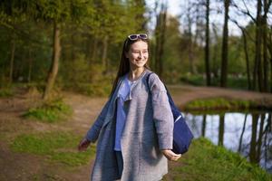 a girl with sunglasses and a bag walks in a forest park near the lake photo