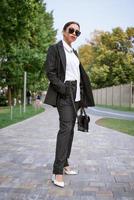 Stylish businesswoman posing on the street in suit and bag in hand photo