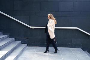 Businesswoman in coat with a bag in her hands goes up the steps to the building photo