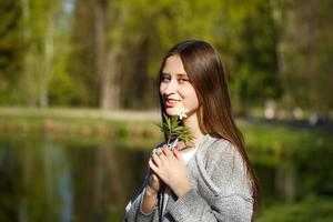 retrato de una niña en el fondo de un parque con un lago, sosteniendo una flor de bosque salvaje. foto