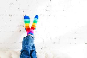 Women's legs in rainbow socks against a white brick wall background. Concept photo