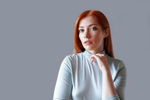 mujer joven contemplativa con largo cabello rojo y cuello alto azul claro foto