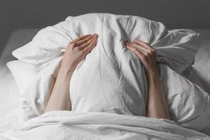 woman in bed hiding face under pillow photo