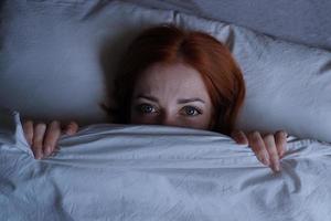 sleepless woman lying in bed hiding under duvet at night photo