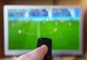 hand pointing remote control at tv with soccer or football match photo