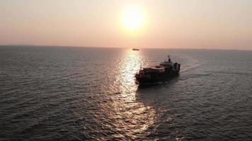 antenne in vooraanzicht van vrachtschip met container en rennen voor exportgoederen van vrachtwerfhaven naar aangepast oceaanconcepttechnologietransport bij zonsondergang. video