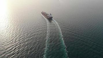 Aerial top view stern of smart cargo ship carrying container and running very fast for export cargo from container yard port to custom ,Contrail line in the ocean by large ship very fast.