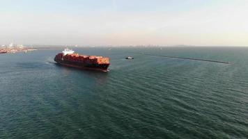 Vista aerea della nave da carico che trasporta container e funziona con un rimorchiatore per l'esportazione di merci sul mare di vongole dal porto del cantiere di carico al trasporto di merci oceanico personalizzato via nave. video