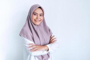 una joven islámica asiática que lleva un pañuelo en la cabeza tiene las manos cruzadas con una sonrisa feliz y confianza. mujer islámica indonesia exitosa de fondo gris foto