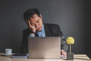 hombre de negocios asiático que se queda dormido en el escritorio de la oficina con los ojos cerrados, joven con exceso de trabajo, trabajador desmotivado durmiendo en el lugar de trabajo, aburrido del trabajo de rutina