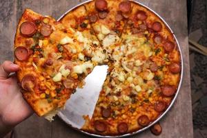 Top view of hand holding meat lover pizza slices . Traditional italian cuisine, delicious fast food. Savory dish with salami and cheese on wooden table. Tasty pizzeria meal on plate. photo