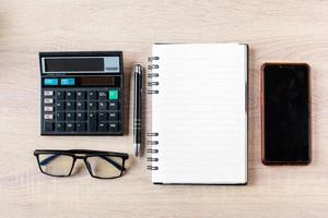 Flat lay, top view of businessman accessories on wooden office desktop with calculator, eyeglasses, pen,book and smart phone photo