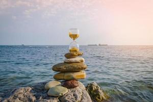 An hourglass with golden sand on sea rocks against a blue sea background. photo