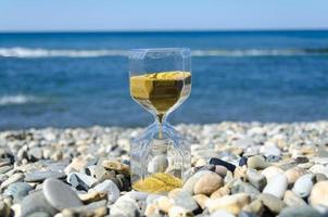 An hourglass with golden sand on the shore against the blue sea photo