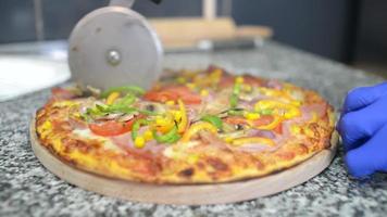 um cozinheiro corta uma pizza quente fresca em pedaços em uma cozinha video