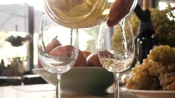 um homem derramando um vinho branco em um copo sobre uma mesa de uma vinícola
