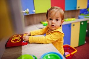 linda niña jugando en el centro de juegos interior. sala de juegos de jardín de infantes o preescolar. prepara la comida en la estufa en la cocina de los niños. foto