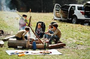 Family bonfire in mountain. Frying sausages. Mother with four kids camping. Autumn hike and camp weather. Warming and cooking near flame together. photo