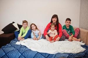 Happy big family is having fun together in bedroom. Large family morning concept. Mother with four kids wear pajamas in bed at home. photo