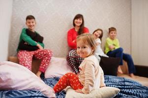 la gran familia feliz se está divirtiendo juntos en el dormitorio. gran concepto de mañana familiar. madre con cuatro hijos usa pijama en la cama en casa. foto