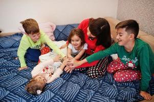 la gran familia feliz se está divirtiendo juntos en el dormitorio. gran concepto de mañana familiar. madre con cuatro hijos usa pijama en la cama en casa. foto