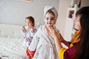 Mother with daughters in a bathrobe with a towel on her head take care of the skin at home, cucumbers on eyes. photo